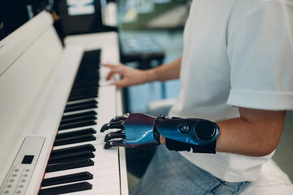 Молодой инвалид играет на фортепиано электронном синтезаторе с искусственной рукой в музыкальном магазине. — стоковое фото