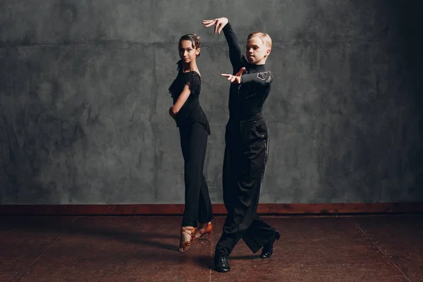 Casal jovem homem e mulher de vestido preto dançando em dança de salão rumba. — Fotografia de Stock