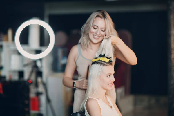 Cabeleireiro feminino fazendo extensões de cabelo para jovem mulher com cabelo loiro no salão de beleza. Extensão profissional do cabelo. — Fotografia de Stock