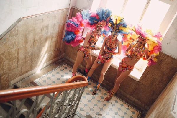 Женщина в бразильском костюме карнавала самбы с красочными перьями оперения расслабиться в старом входе с большим окном — стоковое фото