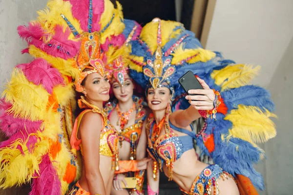 Mujer en traje de carnaval de samba brasileña con plumas de colores plumaje con teléfono móvil tomar selfie en la antigua entrada con ventana grande —  Fotos de Stock