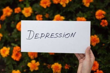 Kadın elinde çiçek arkaplanındaki depresyon sözcüğüyle beyaz bir kağıt tutuyordu.