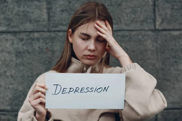 Mädchen hält Blatt Papier mit Wort Depression in der Hand. Frau mit Kopfschmerzen berührt Kopf — Stockfoto