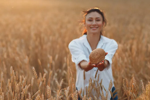 Donna che tiene il pane di grano fatto in casa nelle mani nel campo di grano al tramonto. — Foto Stock