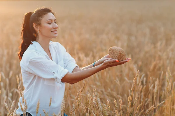 Donna che tiene il pane di grano fatto in casa nelle mani nel campo di grano al tramonto. — Foto Stock