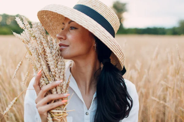Giovane donna in cappello di paglia che tiene covone di spighe di grano in campo agricolo — Foto Stock
