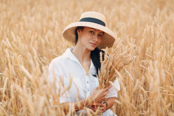 밀짚모자를 쓴 젊은 여자 가 농지에서 밀 귀 단을 들고 있다 — 스톡 사진