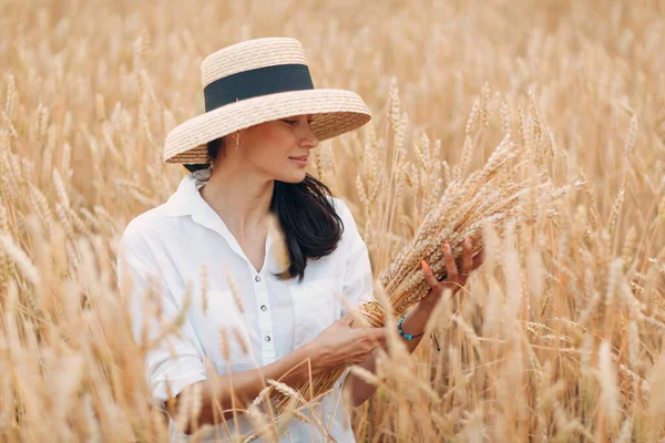 Giovane donna in cappello di paglia che tiene covone di spighe di grano in campo agricolo — Foto Stock