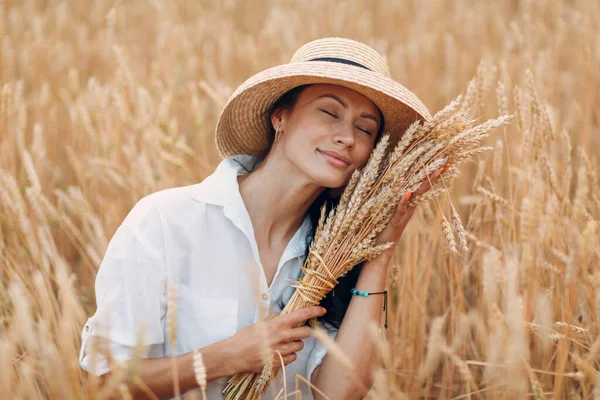 Giovane donna in cappello di paglia che tiene covone di spighe di grano in campo agricolo — Foto Stock