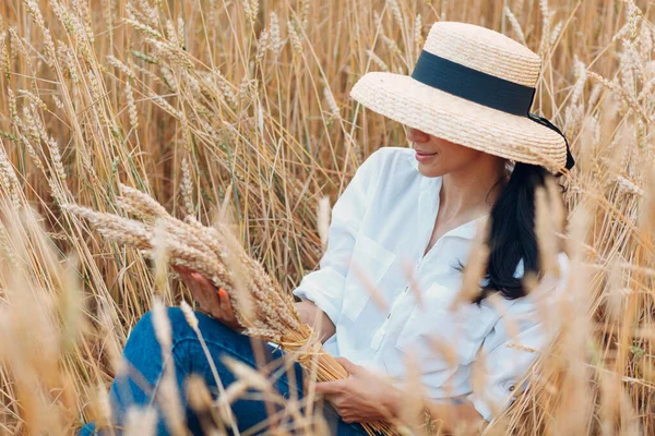 Giovane donna in cappello di paglia che tiene covone di spighe di grano in campo agricolo — Foto Stock