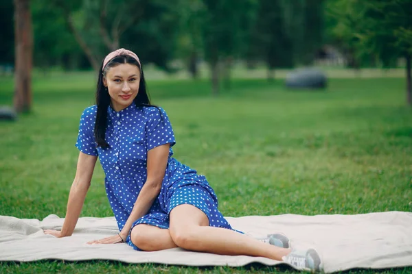 Όμορφη νεαρή ενήλικη γυναίκα σε μπλε φόρεμα πικνίκ κάθεται στο λιβάδι στο πάρκο — Φωτογραφία Αρχείου