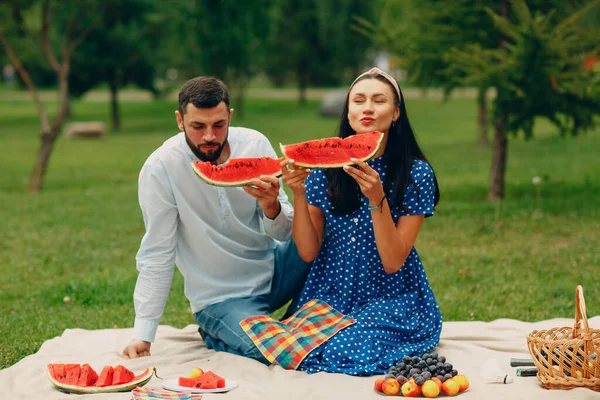 Junge erwachsene Frau und Mann picknicken auf der grünen Wiese im Park und amüsieren sich mit Wassermelone — Stockfoto