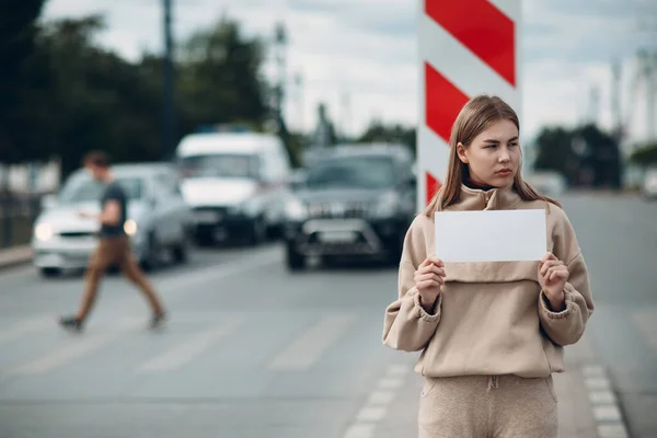 Une jeune femme tient une affiche en papier blanc à la main. Fille avec blanc feuille de modèle vierge dans les mains. — Photo