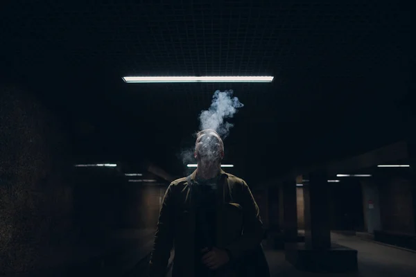 Retrato de un joven caucásico fumando cigarrillo electrónico en la oscuridad con luz de línea — Foto de Stock