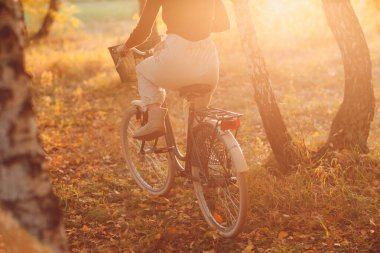 Günbatımında sonbahar parkında bisiklet süren mutlu aktif genç kadın.
