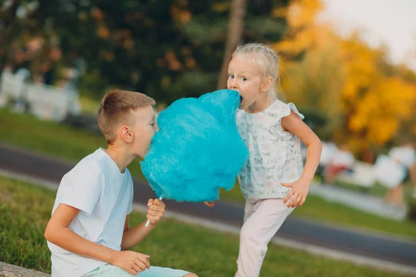 Happy children boy and girl eating blue cotton candy outdoors — Stock Photo, Image