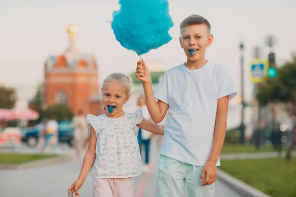 Happy children boy and girl eating blue cotton candy outdoors — Stock Photo, Image