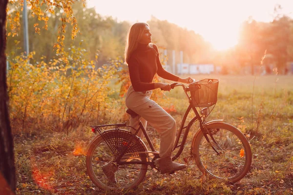 Feliz jovem ativo montando bicicleta vintage no parque de outono ao pôr-do-sol — Fotografia de Stock