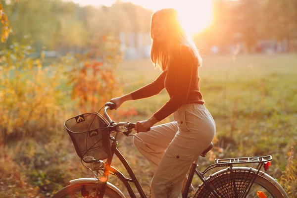 Feliz jovem ativo andando de bicicleta vintage com cesta no parque de outono ao pôr do sol — Fotografia de Stock