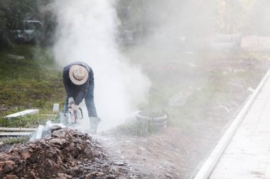 İşçi ustası kaldırımı dairesel testereyle keserken kaldırımı onarıyor.