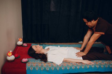 Taylandlı adam güzellik merkezinde genç bir kadına klasik Tayland masajı yapıyor.