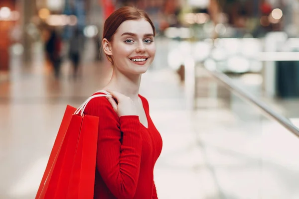 Mujer joven con bolsas rojas de papel en el centro comercial. Viernes Negro y San Valentín concepto de día —  Fotos de Stock