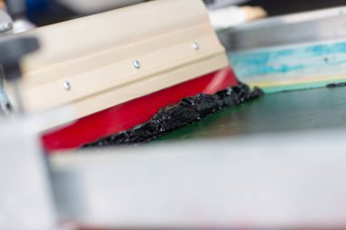 Giyim fabrikasında seri ipek ekran baskı işlemi. Çerçeve, cam sileceği ve plastisol rengi