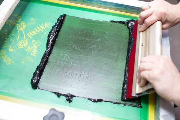 Serigraphy silk screen print process at clothes factory. Frame, squeegee and plastisol color paints