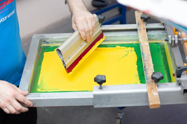 Serigraphy silk screen print process at clothes factory. Frame, squeegee and plastisol color paints