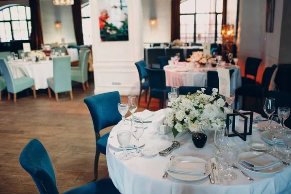 Mesas redondas no restaurante com toalhas de mesa brancas e buquês brancos de decoração de flores — Fotografia de Stock
