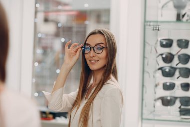 Alışveriş merkezinin gözlükçü köşesinde gülümseyen ve bardakları seçen muhteşem genç bayanı yakından çek. Optometriste gözlük alan mutlu güzel bir kadın.