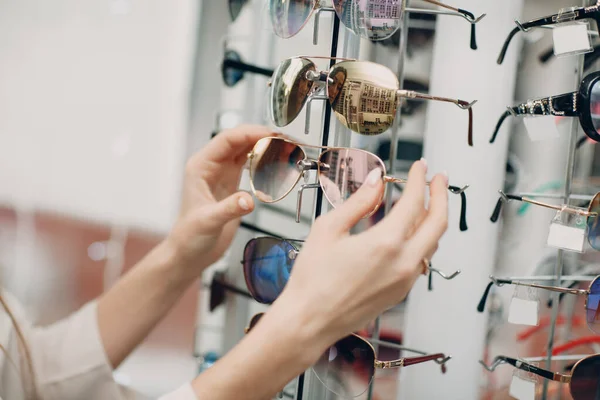 Primer plano de la hermosa joven sonriente que sonríe recogiendo y eligiendo gafas en la esquina óptica en el centro comercial. Feliz hermosa mujer comprando gafas de vista en el optometrista — Foto de Stock