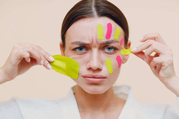 Beautiful woman applying tape lifting treatment on face