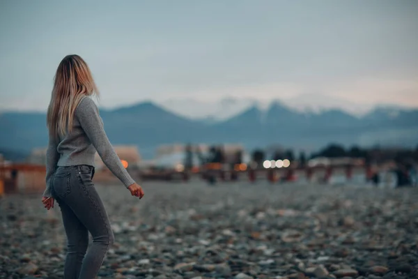Jeune femme vêtue de jeans et pull sur la plage de galets au bord de la mer. — Photo