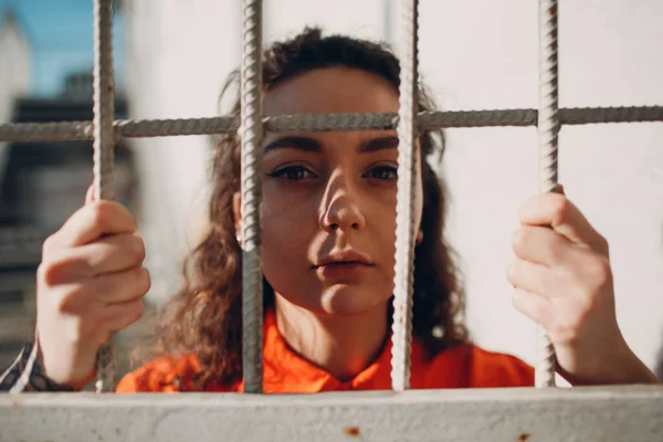 Wanita muda berjas oranye di balik jeruji penjara. Perempuan dalam warna-warni keseluruhan potret. Konsep hukum dan keadilan. — Stok Foto