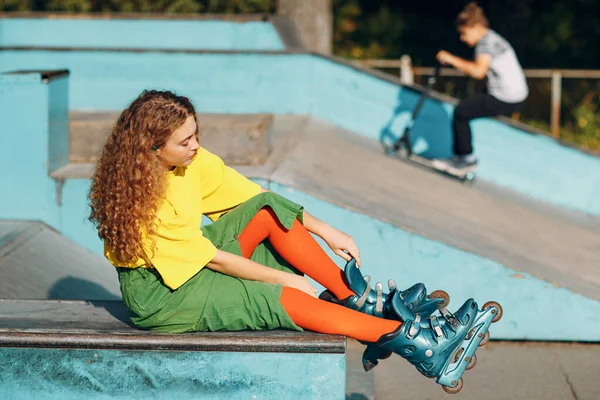 Junge Frau in grünen und gelben Klamotten und orangefarbenen Strümpfen mit lockiger Frisur beim Rollschuhlaufen im Skatepark — Stockfoto