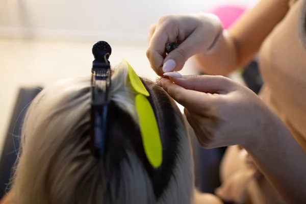 Cabeleireiro feminino fazendo extensões de cabelo para jovem mulher com cabelo loiro no salão de beleza. Extensão profissional do cabelo. — Fotografia de Stock