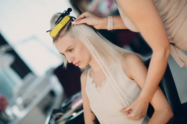 Cabeleireiro feminino fazendo extensões de cabelo para jovem mulher com cabelo loiro no salão de beleza. Extensão profissional do cabelo fio. — Fotografia de Stock