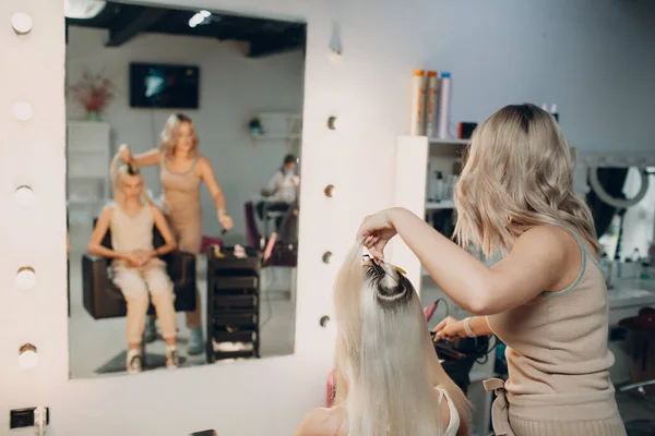 Cabeleireiro feminino fazendo extensões de cabelo para jovem mulher com cabelo loiro no salão de beleza. Extensão profissional do cabelo. — Fotografia de Stock
