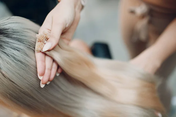 Kapper vrouwelijke het maken van hair extensions aan jonge vrouw met blond haar in schoonheidssalon. Professionele hair extension streng van haar. — Stockfoto
