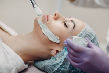 Genç bir kadın güzellik merkezine kilden bir maske takıyor.