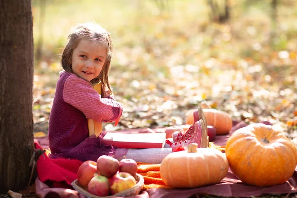 Cute little girl w jesiennym parku z książkami i pomarańczowy kolor liści i żółty dyni. — Zdjęcie stockowe