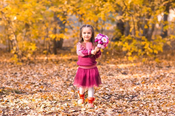 Cute little girl w jesiennym parku z różowym bukietem kwiatów — Zdjęcie stockowe