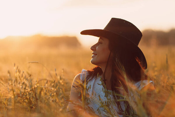 Woman farmer in cowboy hat profile portrait at agricultural field on sunset