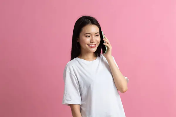 Sorrindo mulher asiática falando telefone celular de pé no fundo rosa. — Fotografia de Stock