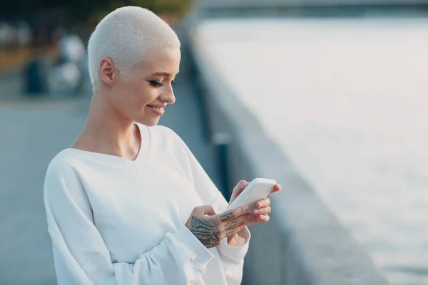 Тысячелетняя молодая женщина блондинка короткие волосы открытый улыбающийся портрет с сотовым телефоном — стоковое фото