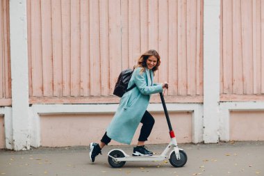 Şehirde mavi ceketli, elektrikli scooterlı genç bir kadın var.