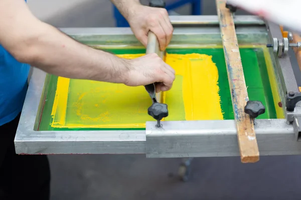 Serigraphy silk screen print process at clothes factory. Frame, squeegee and plastisol color paints