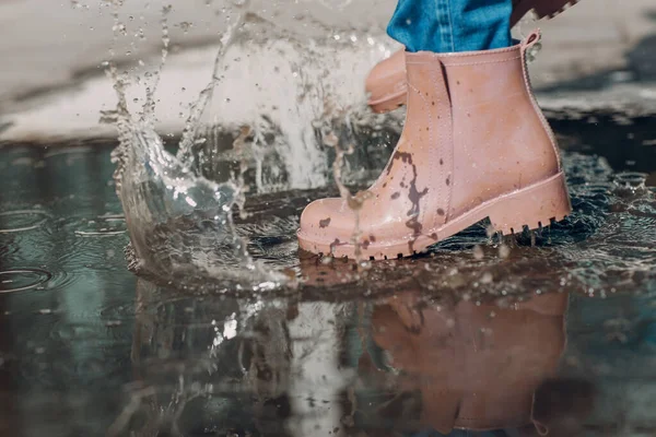 Femme portant des bottes en caoutchouc de pluie marchant en courant et sautant dans la flaque d'eau avec éclaboussure et gouttes sous la pluie d'automne — Photo