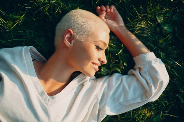 Millenial junge Frau blonde kurze Haare im Freien lächelnd lag auf Gras Porträt. — Stockfoto